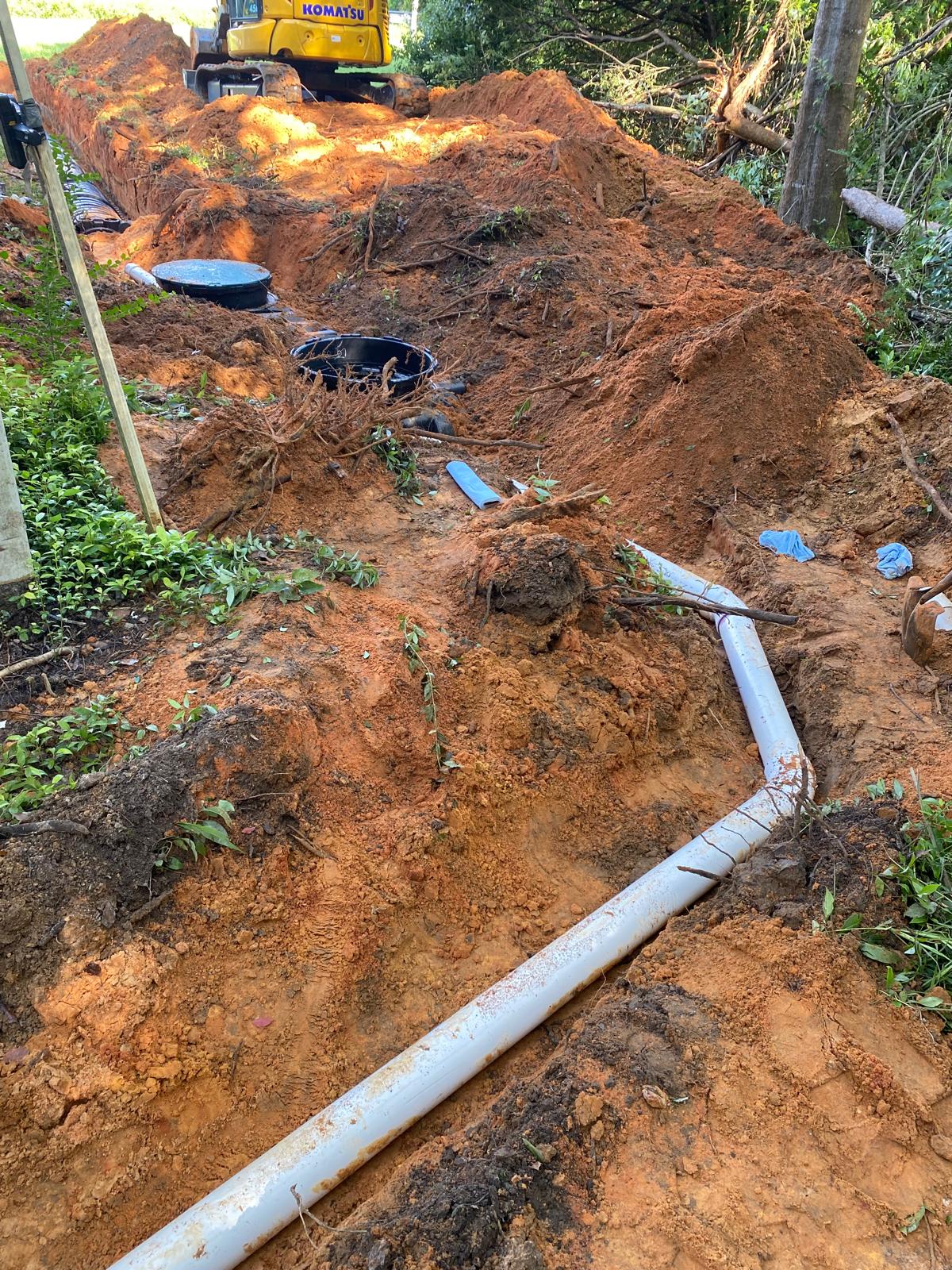 Excavator bucket dropping dirt into an open trench.
